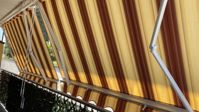 Striped yellow and brown awning partially extended over a balcony railing.
